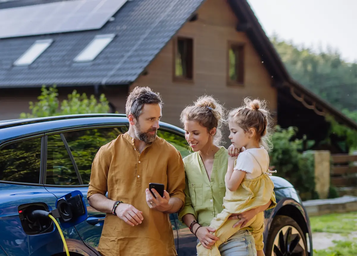 Familie lädt ein Elektroauto an einer Ladestation vor ihrem Haus und schaut gemeinsam auf ein Smartphone