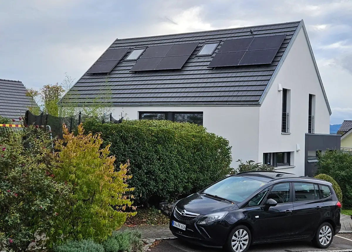 Photovoltaikanlage auf dem Dach eines modernen Einfamilienhauses mit geparktem Auto im Vordergrund