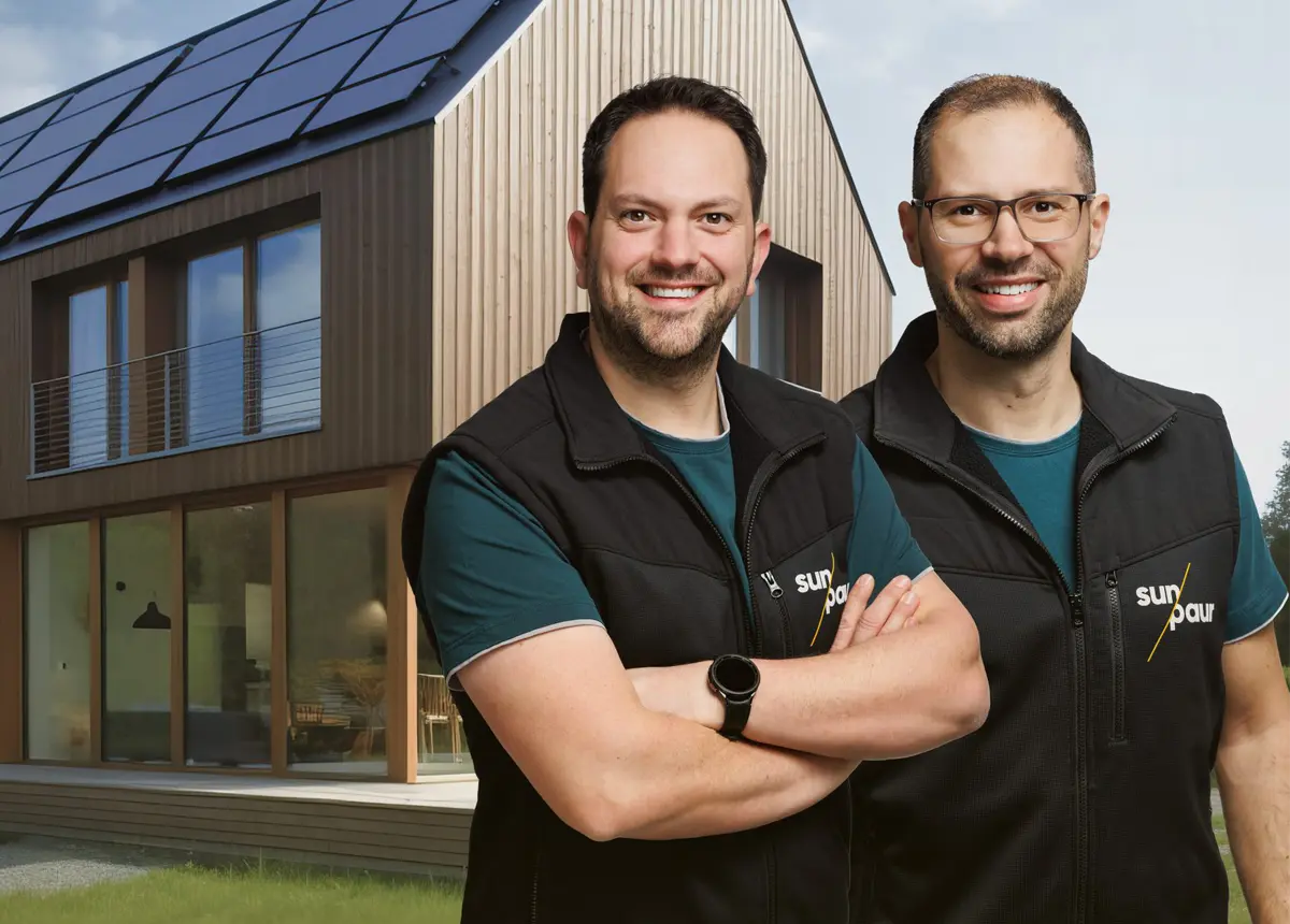 Zwei Solarinstallateure stehen vor einem modernen Haus mit Photovoltaikanlage auf dem Dach